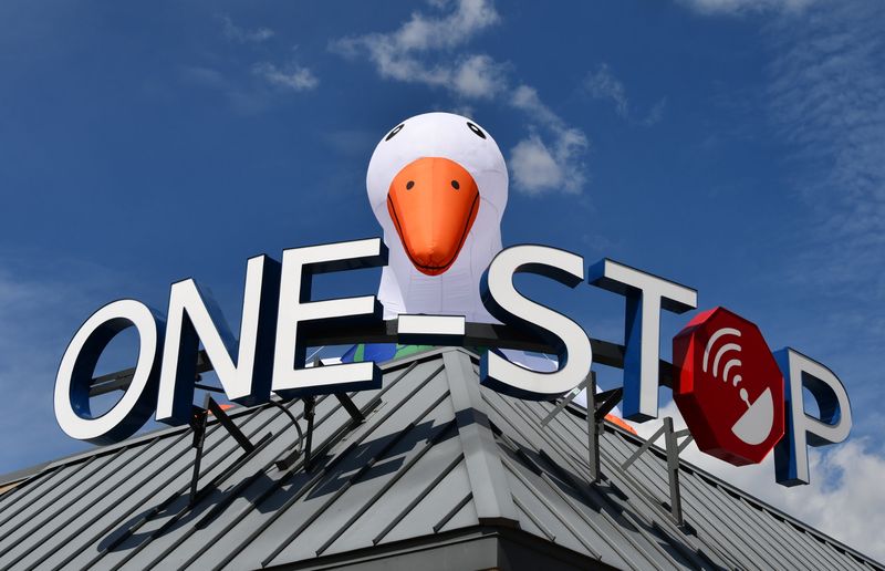 A giant inflatable goose peeking over the One-Stop sign on the office roof against a blue sky